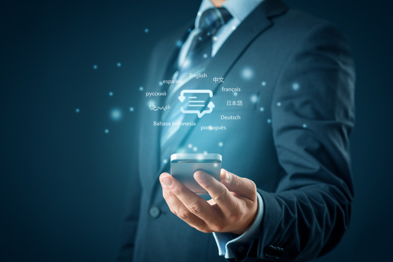 A businessman in a suit holds a smartphone from which various language symbols light up, including English, German, French, Spanish, and others. This symbolizes global communication and translation in an international business environment, fitting the theme of efficient and precise translations in companies.